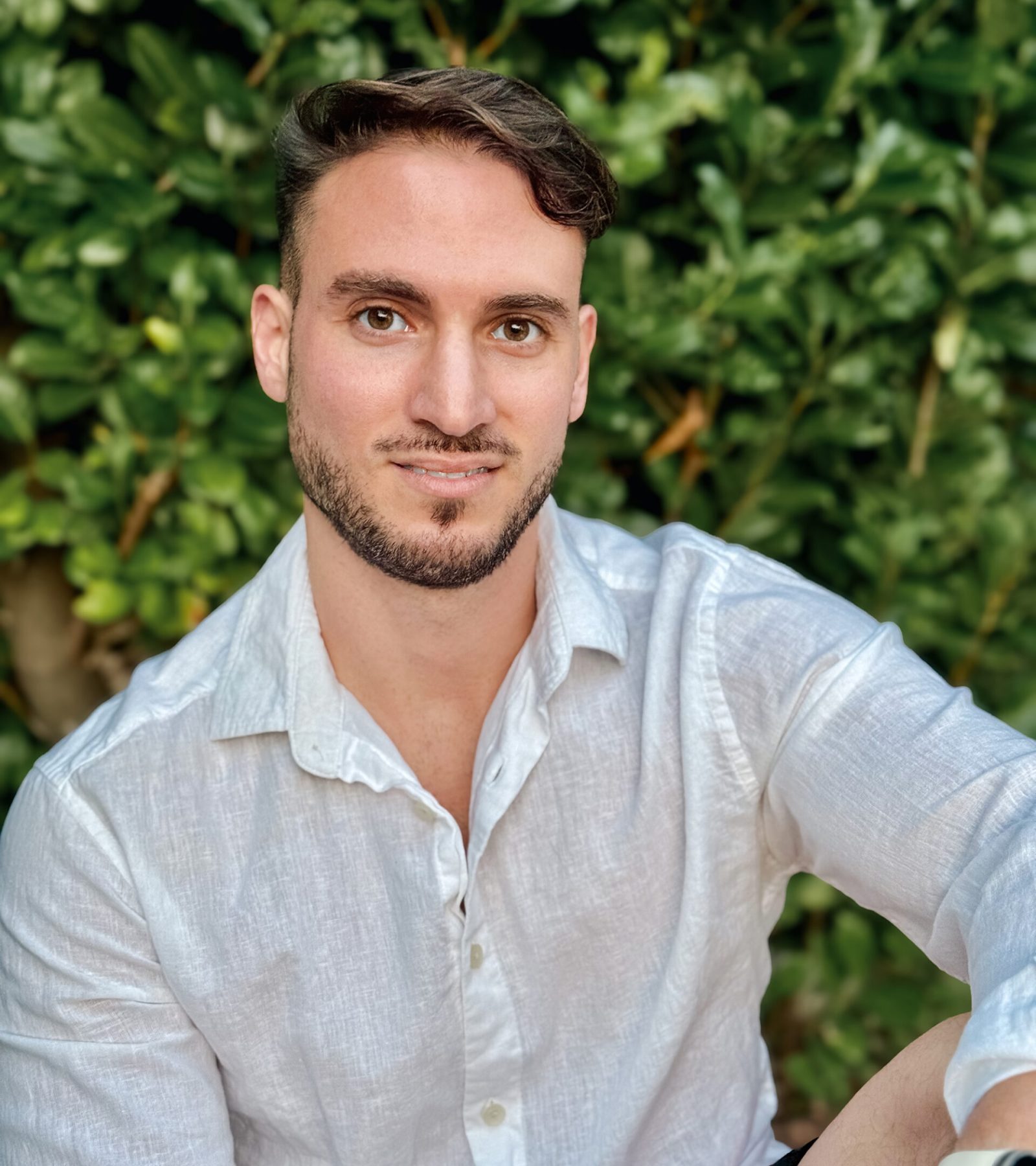 Myself smiling warmly in a serene forest setting, surrounded by lush green trees. Sunlight filters through the branches, illuminating their joyful expression. Vibrant leaves and a gentle breeze create a peaceful, natural atmosphere.